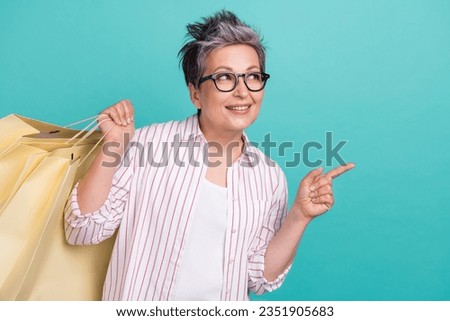 Photo of cheerful mature lady direct finger empty space interested fashion designers updates hold bargain isolated on cyan color background