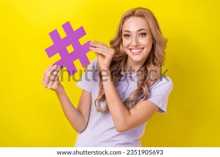 Photo of toothy beaming cute girl with curly hairstyle wear violet polo hands hold hashtag symbol isolated on yellow color background