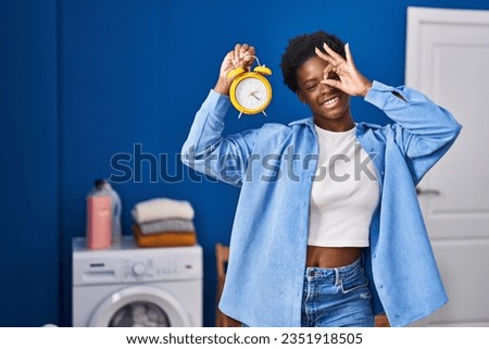 African american woman waiting for laundry smiling happy doing ok sign with hand on eye looking through fingers 