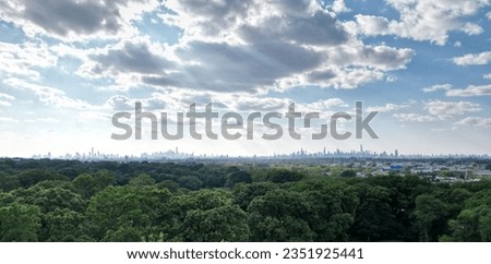 aerial view of nyc skyline in the distance (far away shot of manhattan from queens with dramatic sunny sky) drone photo, from above trees, urban cityscape new york city downtown midtown forest park