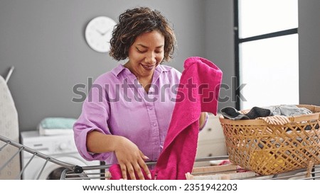 Young beautiful latin woman smiling confident hanging clothes on clothesline at laundry room