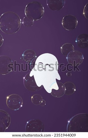 Cute paper ghost with smile in soap bubbles on purple background