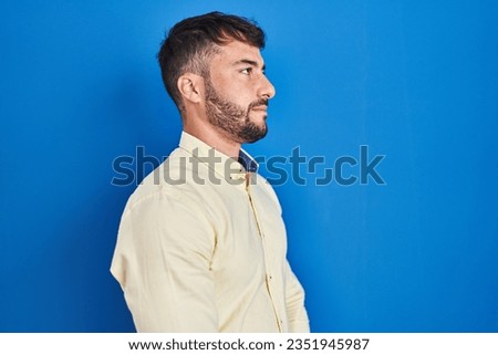 Handsome hispanic man standing over blue background looking to side, relax profile pose with natural face and confident smile. 