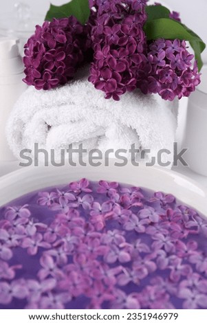 Lilac flowers with white towel and bowl of aromatic water on table, closeup