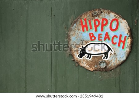 HIPPO BEACH RETRO VINTAGE SIGN -  Large fat hand painted illustration picture image of a hippopotumus animal offset signpost with fun bright colored old text signage and palm tree background
