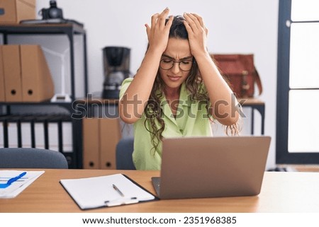Young hispanic woman working at the office wearing glasses suffering from headache desperate and stressed because pain and migraine. hands on head.  Royalty-Free Stock Photo #2351968385