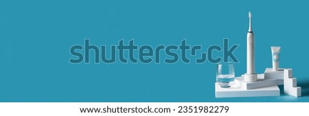 Basic oral hygiene concept. Electric Toothbrush with tube of toothpaste and glass on water on the podiums on blue background. Banner with Copy space