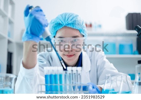 Female scientist in laboratory expertly wields use pipette dripping blue substance with focus on biology, medicine, and biotechnology, research involves careful analysis, experiments, and discoveries.