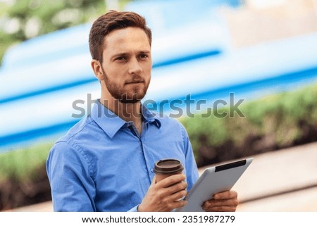 Ginger businessman working outdoors on his tablet with his coffee