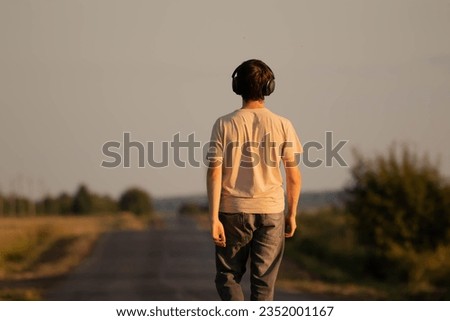 A teenager walks along the road in headphones. A teenager listens to music with headphones.