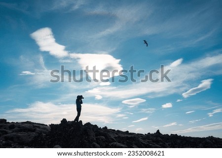 Silhouette of photographer standing with camera taking a photo on the mountain and bird flying in blue sky