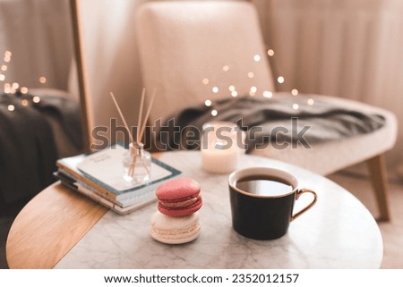 Cup of coffee with macarons and stack of paper books with candle on marble table in bedroom top view closeup. 
