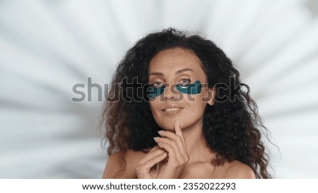 A woman performs a cosmetic procedure. Portrait of a seminude woman with blue patches under the eyes in the studio on a gray background with highlights. Beauty, cosmetology, skin care.