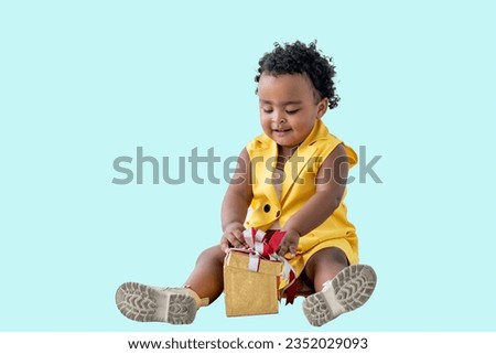Portrait images, A 2-year-old Nigerian baby girl with beautiful curly hair, smiling and happy with gift box, on light blue isolated background. to African baby and gift box concept.