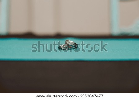 "In a playful twist, wedding rings rest on a pool table's rich green. A symbol of forever love amidst the cues and balls, where elegance meets a touch of whimsy."