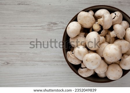Raw White Champignon Mushrooms in a Bowl on a white wooden background, top view.