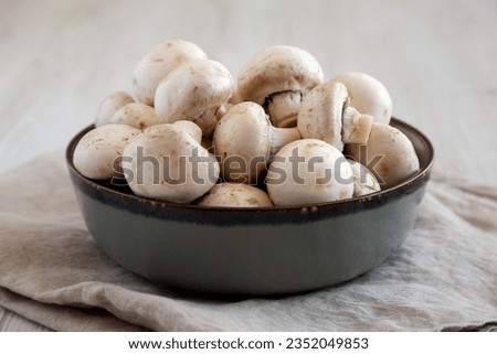 Raw White Champignon Mushrooms in a Bowl on a white wooden background, side view. Close-up. Royalty-Free Stock Photo #2352049853