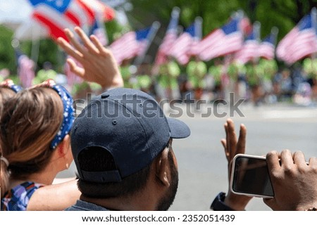 Close up of the heads of two people watching the 4th of July parade in Washington DC waving and taking pictures with parade with American flags out of focus in background
