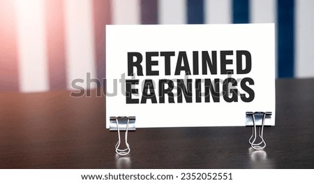 RETAINED EARNINGS sign on paper on dark desk in sunlight. Blue and white background