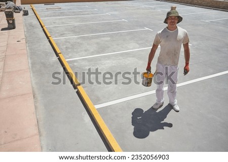 Professional painter at work. Young man uses a paint roller to apply special acrylic paint for road marking on asphalt of a parking lot.	