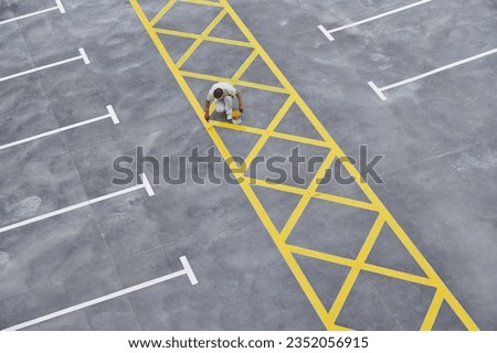 Professional painter at work. Young man uses a paint roller to apply special acrylic paint for road marking on asphalt of a parking lot.	