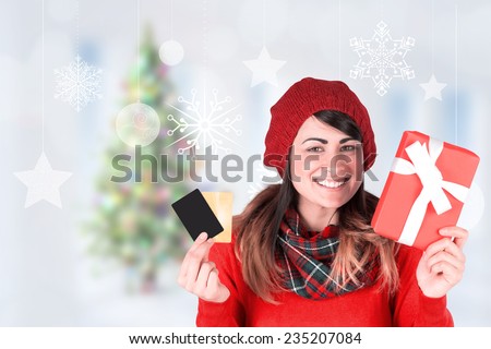 Smiling brunette holding gift and cards against blurry christmas tree in room