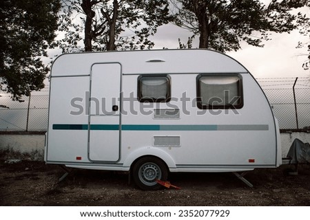 Holiday motor caravan at park camping site. Housing type vehicle is parked on a street in gloomy autumn day. White track car. Mobile home automobile. Vintage caravan monochrome photo.