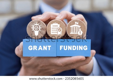 Man holding colorful blocks with icons and inscription: GRANT FUNDING. Concept of grants and funding. Royalty-Free Stock Photo #2352085601