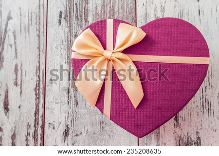 Heart shaped purple gift box with yellow ribbon on white wooden background