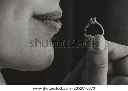 The bride holds a gold ring close to her lips with her fingers, close-up. Morning of the bride. Wedding day. Black and white photo