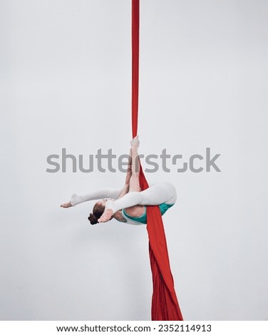 Gymnastics, acrobat and aerial silk with a woman in air for performance, sports and balance. Young athlete person or gymnast hanging on red fabric and white background with space, art and creativity