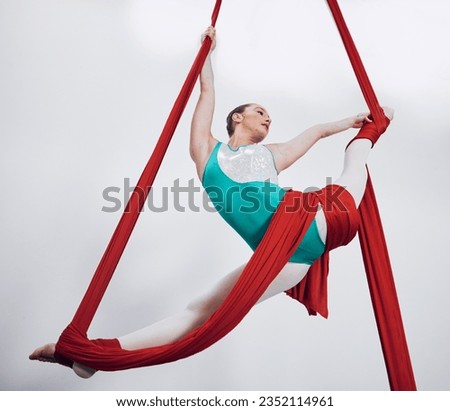 Flexibility, aerial silk and acrobat woman in air for performance, sports and balance. Gymnastics, athlete person or gymnast hanging on red fabric and white background with space, art and creativity