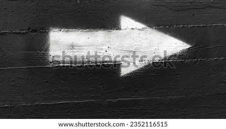 White arrow on a dark gray wall. Black concrete background with white arrow graffiti  Royalty-Free Stock Photo #2352116515