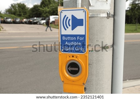 button for audible signal only crosswalk button with illustration of speaker making noise with road behind with pedestrian passing on sidewalk, speaker pointing at them, blue while yellow and black