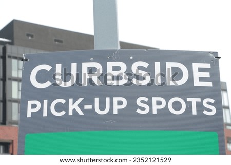curbside pick up spots sign on post with building and sky in background, writing in center frame