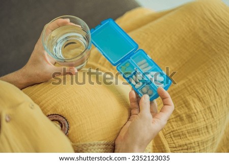 Prenatal Vitamins. Portrait Of Beautiful Smiling Pregnant Woman Holding Pill Box and a glass of water, Taking Supplements For Healthy Pregnancy While Sitting On Couch At Home, Free Space Royalty-Free Stock Photo #2352123035