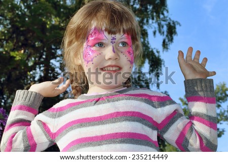 Happy beautiful little girl with pictured purple butterfly on face outdoor