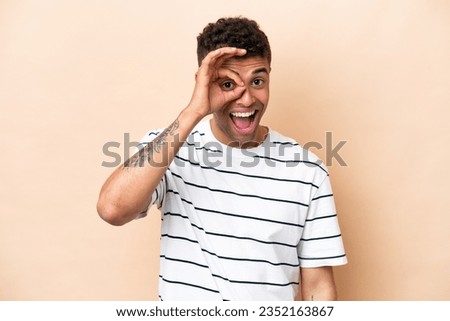Young Brazilian man isolated on beige background showing ok sign with fingers