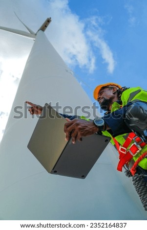 African man workers engineering working with laptop with blue working suit dress and safety helmet in front of wind turbine. Concept of smart industry worker operating of renewable energy.