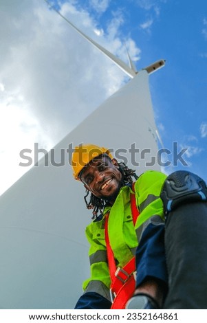 African man workers engineering sitting with confidence with blue working suit dress and safety helmet in front of wind turbine. Concept of smart industry worker operating of renewable energy.
