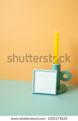 Blue empty picture frame and candle on mint green table. orange wall background. copy space