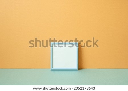 Blue empty picture frame on mint green table. orange wall background. copy space