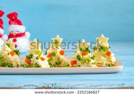 Appetizers in the form of Christmas tree made from cheese, eggs, mayonnaise served with broccoli and pepper pieces over blue wooden background.