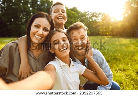 Selfie portrait happy cheerful family spending time in nature. Parents and children having fun in green sunny summer park. Little girl holds camera and takes photo together with mom, dad and brother