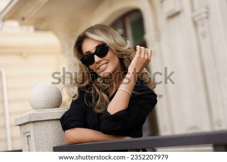 Beautiful smiling blond woman in elegant luxury sunglasses posing on the street. European background. Perfect wavy hairs. Royalty-Free Stock Photo #2352207979