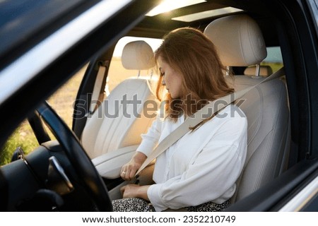 Pretty business lady fastens seat belt in new modern technological car. Happy woman fastening her seatbelt while sitting at the steering wheel of her car. Buckle up and drive safe. Royalty-Free Stock Photo #2352210749