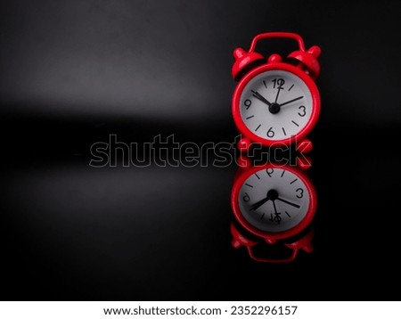 Red alarm clock on black background with reflection on a black acrylic board. Copy and text space.