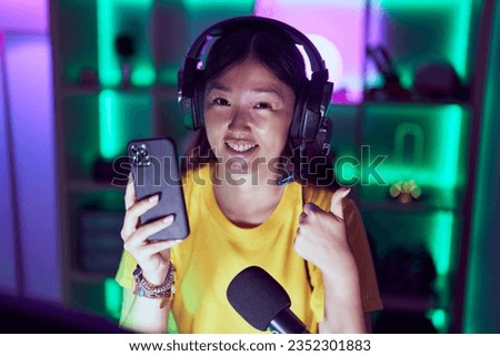 Chinese young woman playing video games with smartphone smiling happy and positive, thumb up doing excellent and approval sign 
