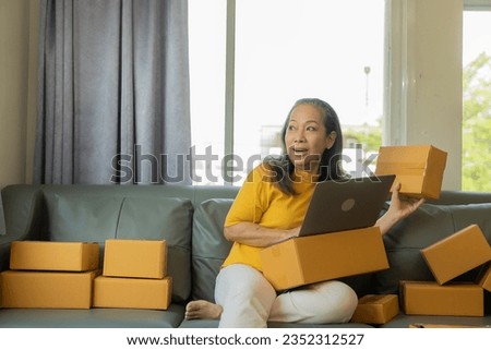 start a small business SME Asian old woman using laptop to receive and check online purchase orders to prepare product boxes Online shopping concept, parcel delivery.
