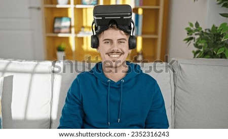 Young hispanic man wearing virtual reality glasses smiling at home